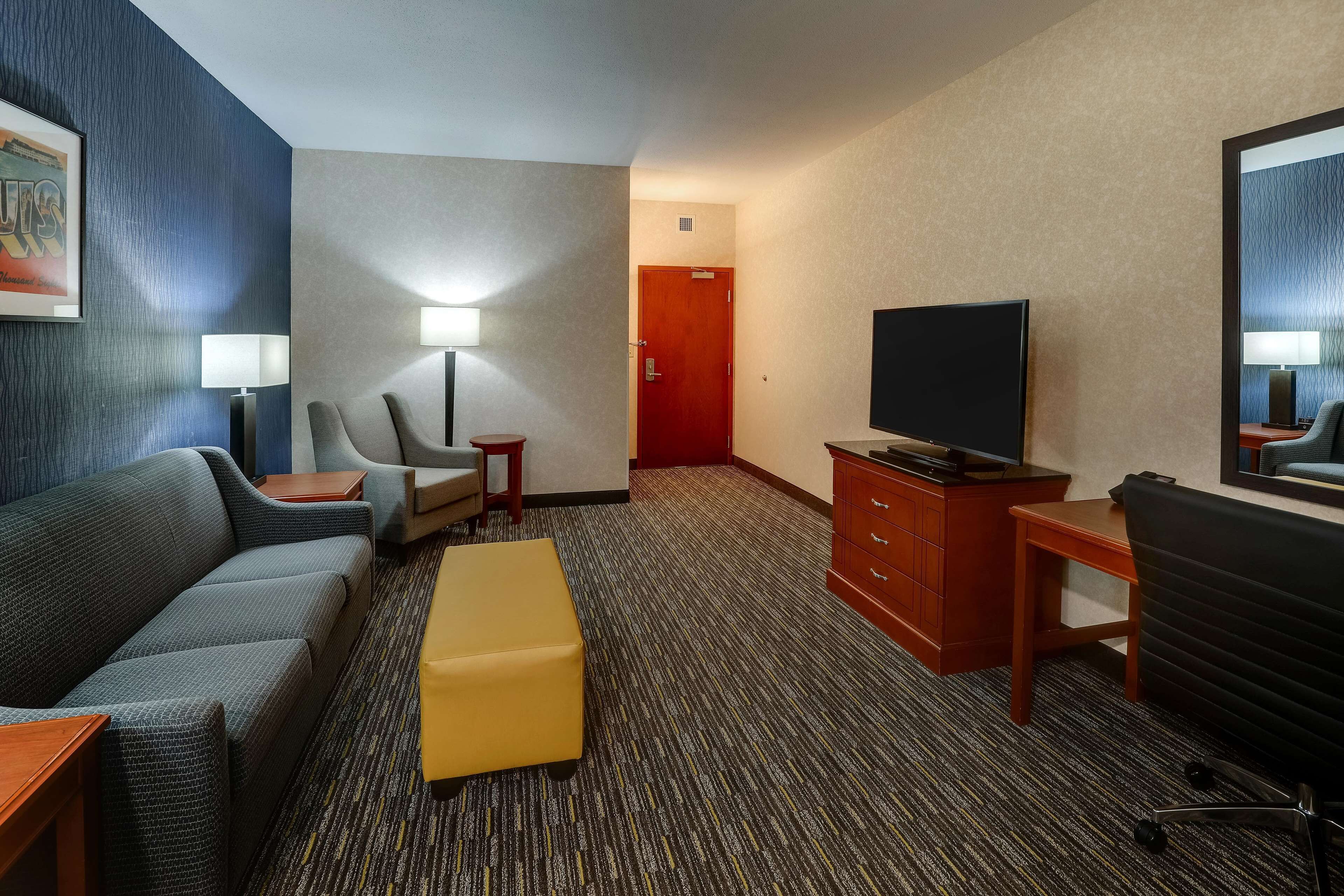 A hotel room with a sofa, a small table, a TV, a desk, and a chair.