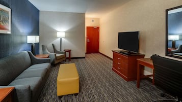 A hotel room with a sofa, a small table, a TV, a desk, and a chair.