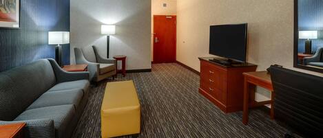 A hotel room with a sofa, a small table, a TV, a desk, and a chair.