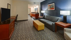 A hotel room with a TV, a sofa, a small table, a lamp, and a carpeted floor.