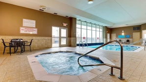 An indoor swimming pool area with a hot tub, a table with chairs, and a sign warning of no lifeguard on duty.