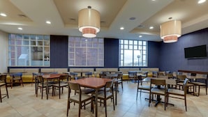 A spacious dining area with multiple tables and chairs, large windows, and ceiling lights.