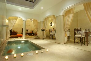 Un área de spa con piscina, velas y una zona de estar con mesa y sillas.