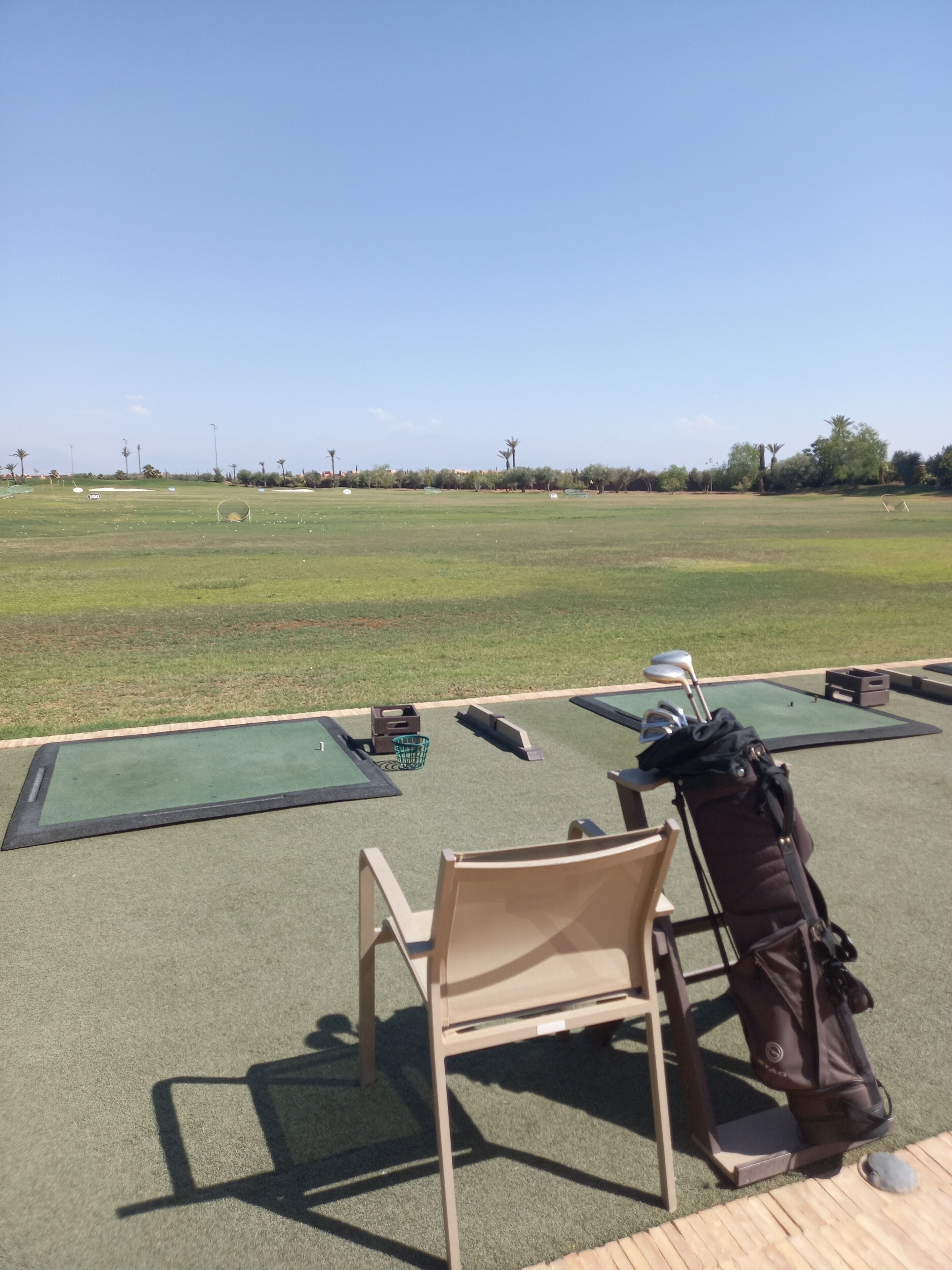 A golf driving range with multiple tee boxes and a seating area with chairs and bags.