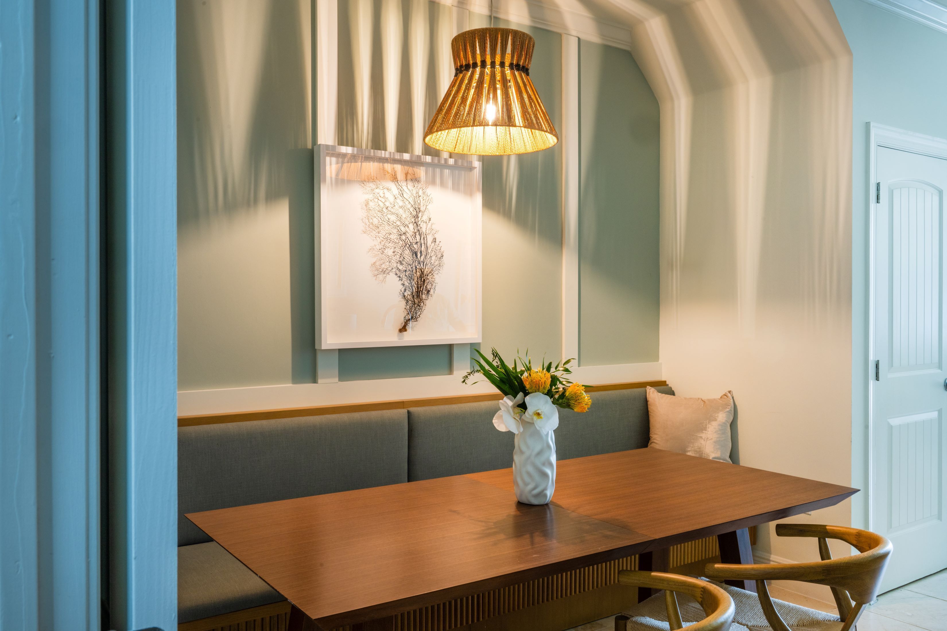 A dining area with a wooden table, cushioned bench, and a vase with flowers.