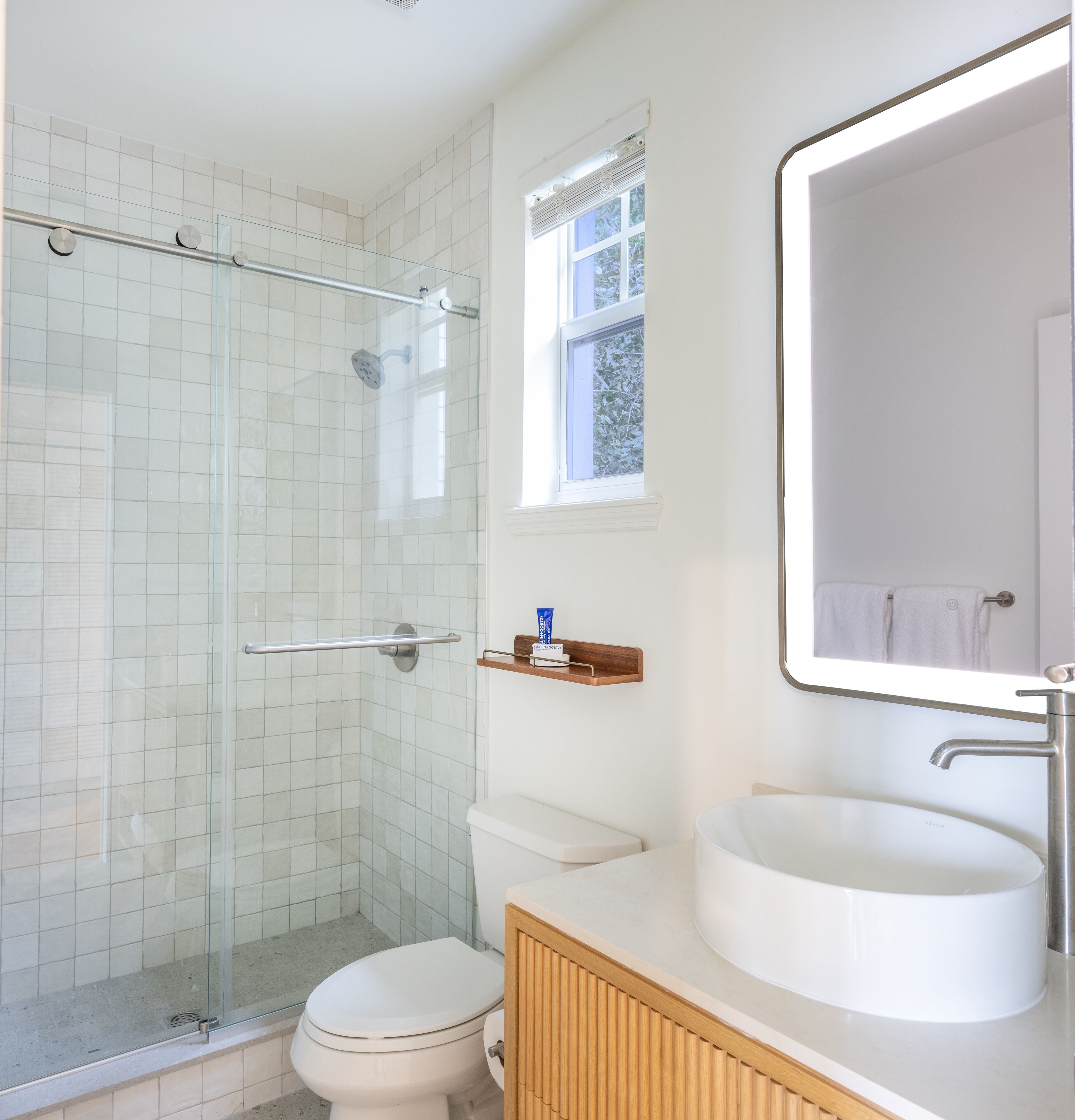 Un baño con ducha de mampara de vidrio, inodoro, lavamanos y espejo.