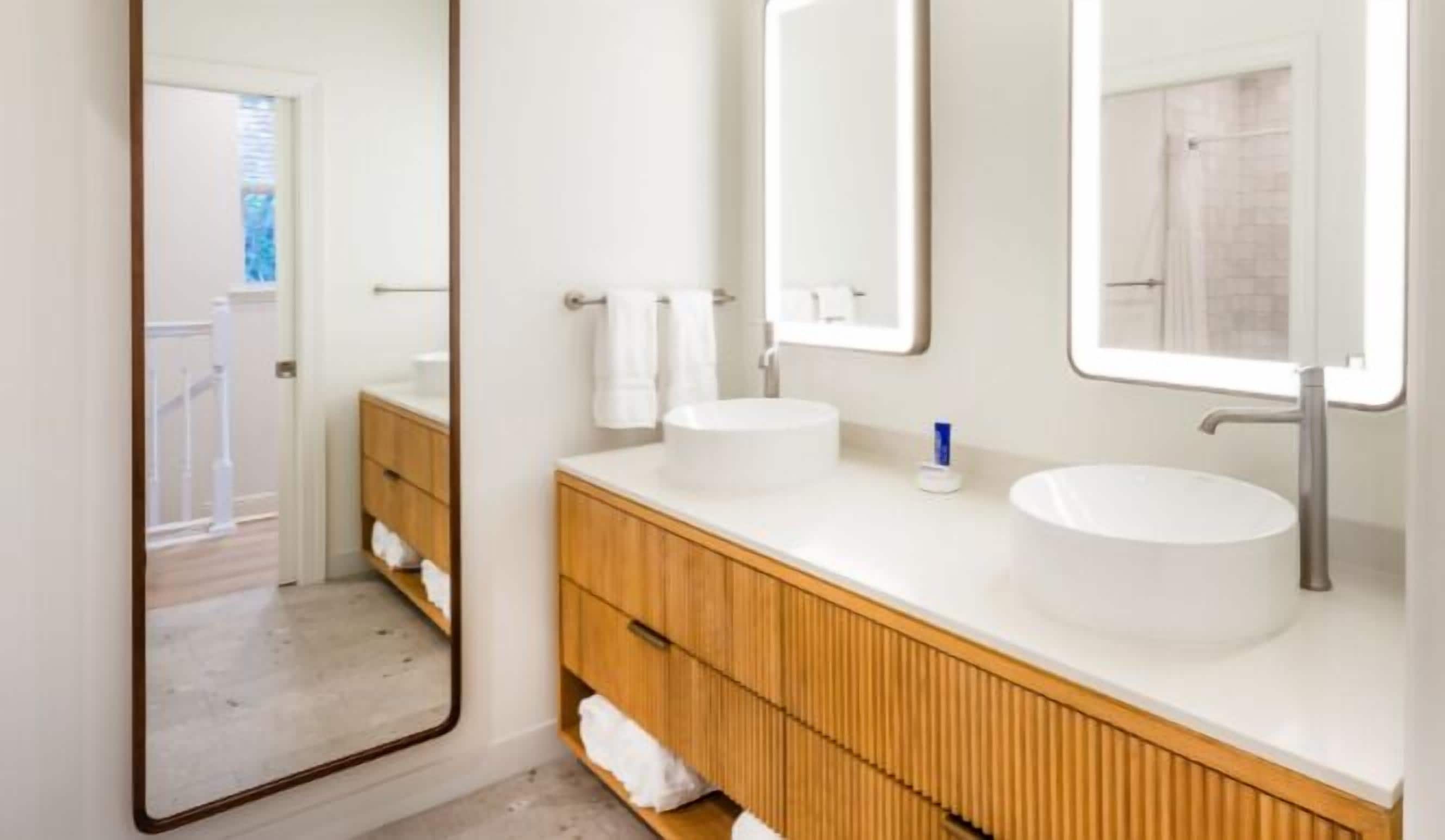 Un baño moderno con dos lavamanos, tocador de madera y un espejo grande.