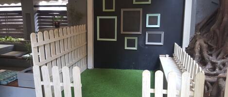 A room with a black wall adorned with framed pictures, a white picket fence, and a green artificial turf area.