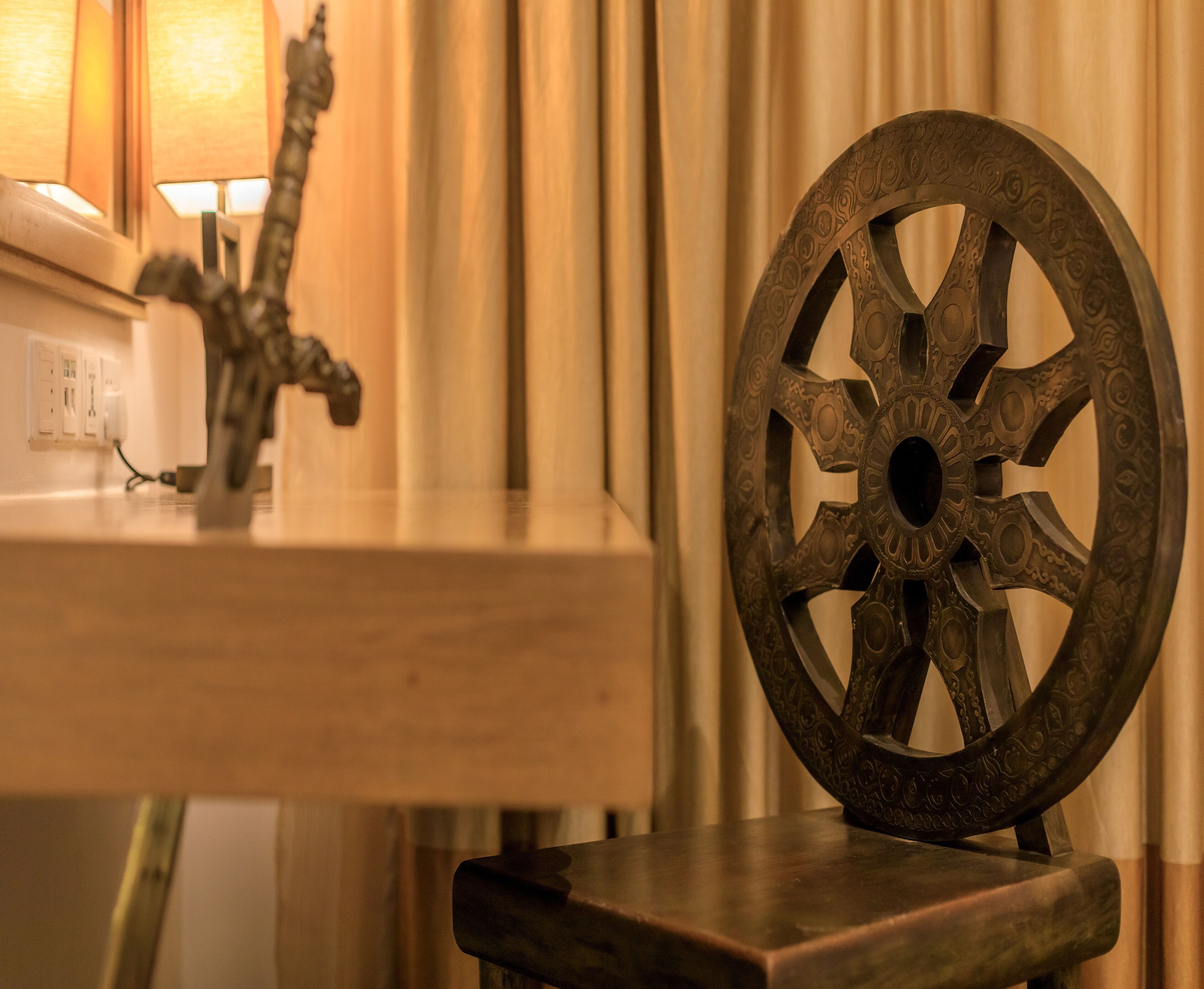 A wooden chair with an ornate metal wheel backrest, a small table with a decorative metal sculpture, and a wall socket.