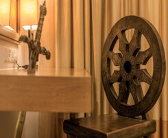 Een houten stoel met een sierlijk metalen rugleuning in wielvorm, een kleine tafel met een decoratieve metalen sculptuur, en een stopcontact.