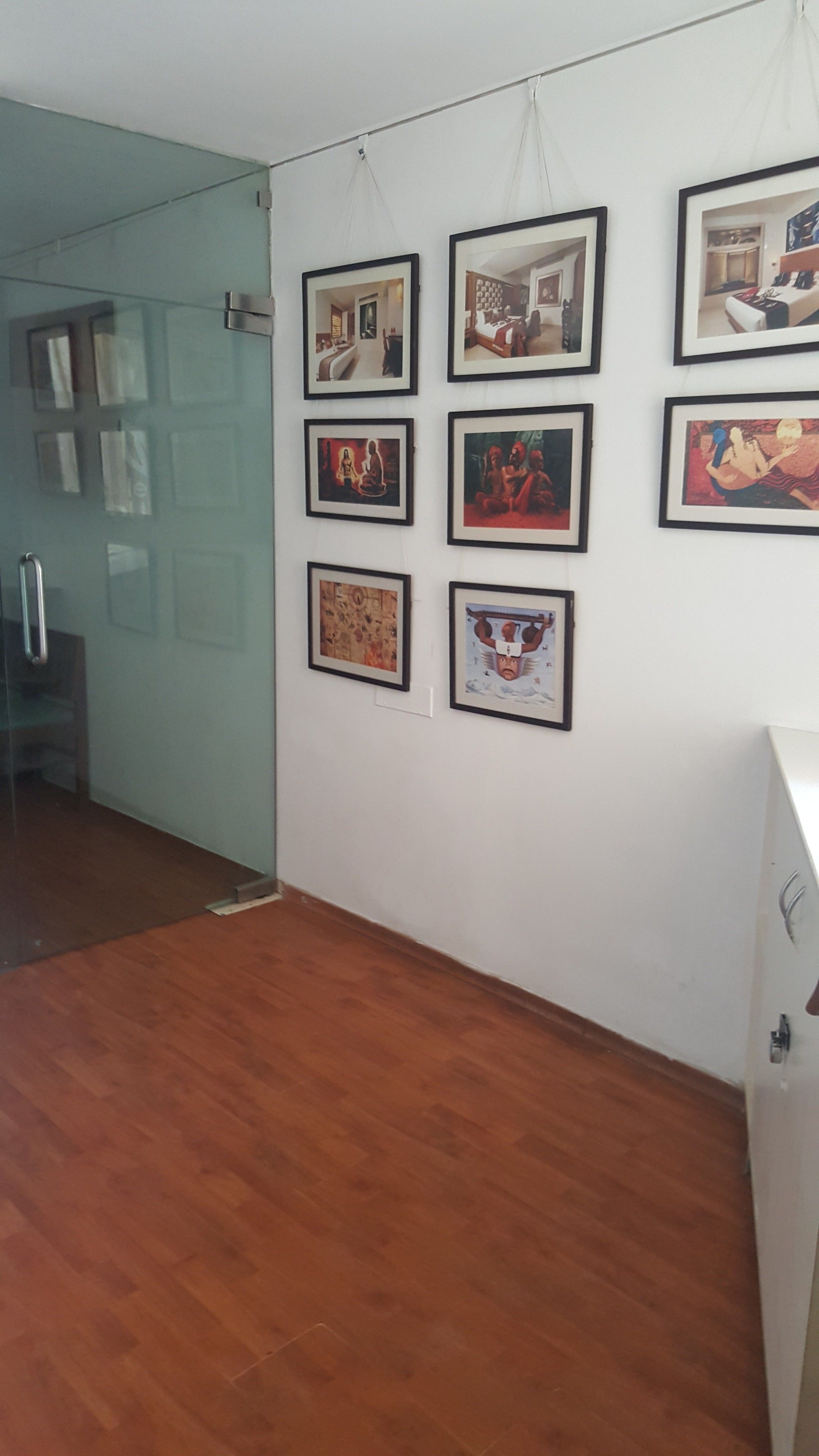 A hallway with framed artwork on the wall and a wooden floor.