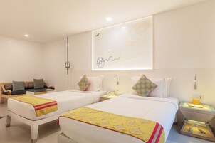 A hotel room with two beds, a sofa, a nightstand, and a wall-mounted artwork.