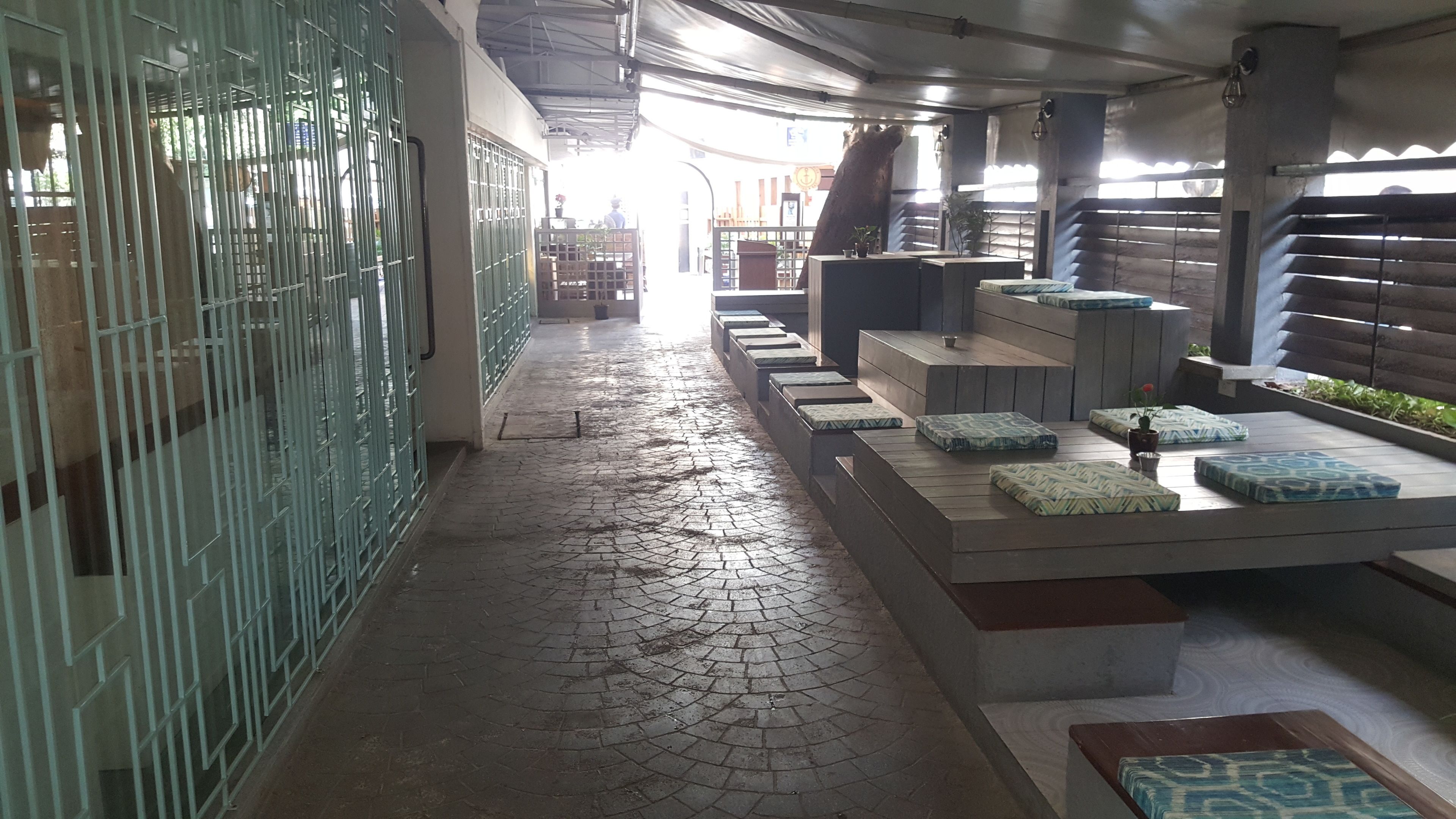 A corridor with a tiled floor, metal gates on one side, and a seating area with cushions and a small table.