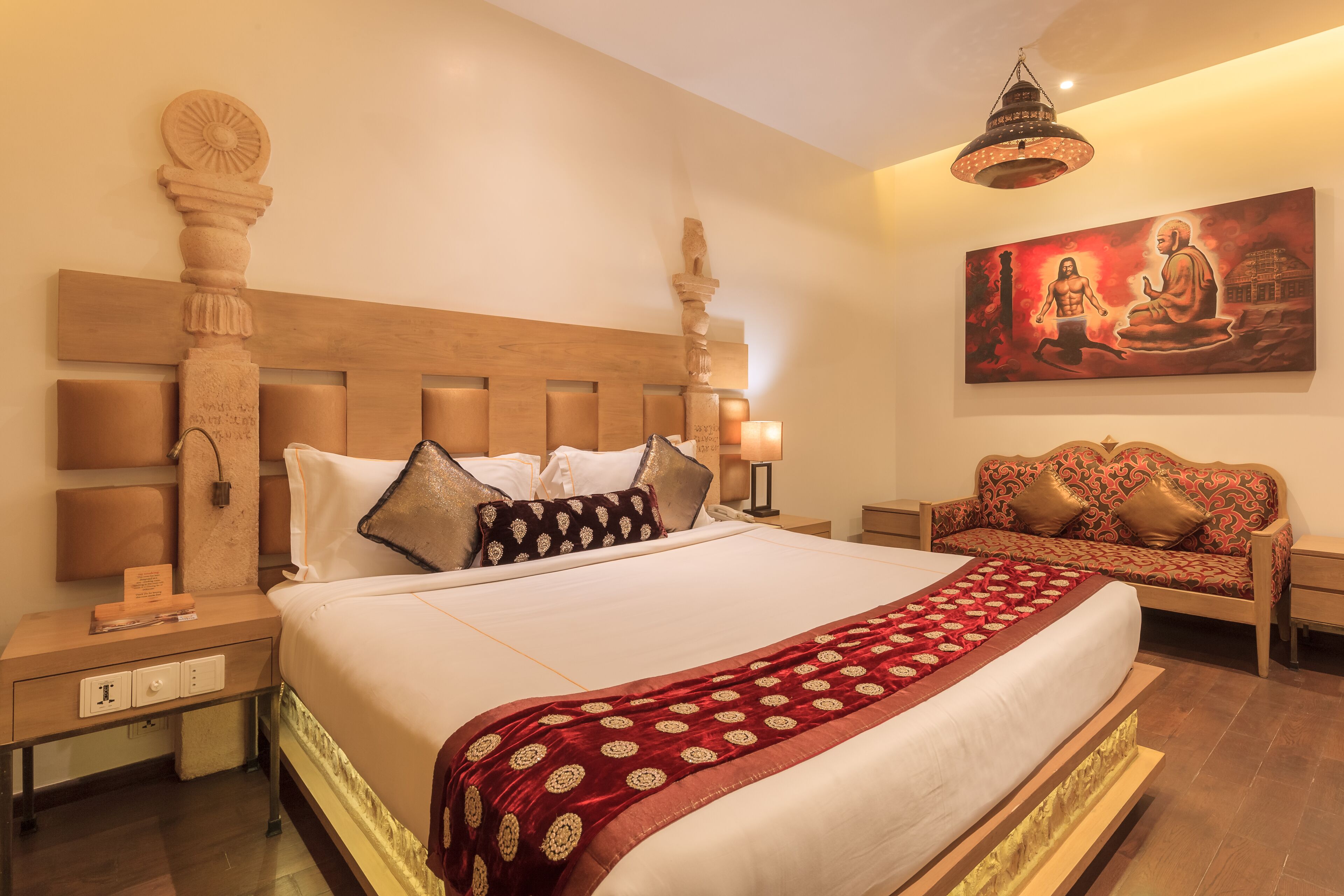 A hotel room with a large bed, wooden headboard, a sofa, and a painting on the wall.