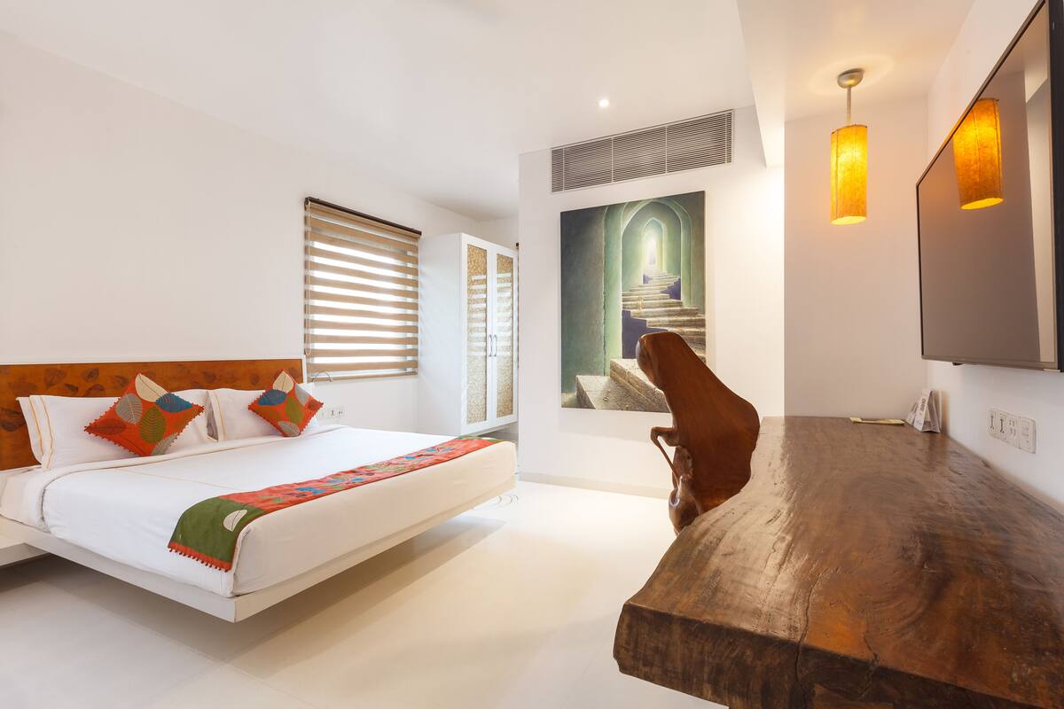 A modern hotel room with a wooden headboard bed, a large mirror, and a wooden dining table.
