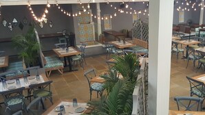 Un restaurante con varias mesas y sillas, luces colgantes y azulejos decorativos en la pared.