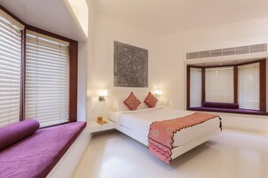 A modern bedroom with a large bed, a window seat, and a decorative wall piece.