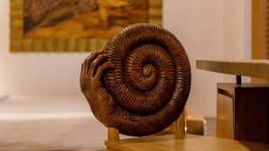 Una escultura espiral de madera sobre una mesa de madera en una habitación con un cuadro en la pared.
