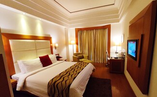 A hotel room with a large bed, a desk with a chair, a television, and a window with curtains.