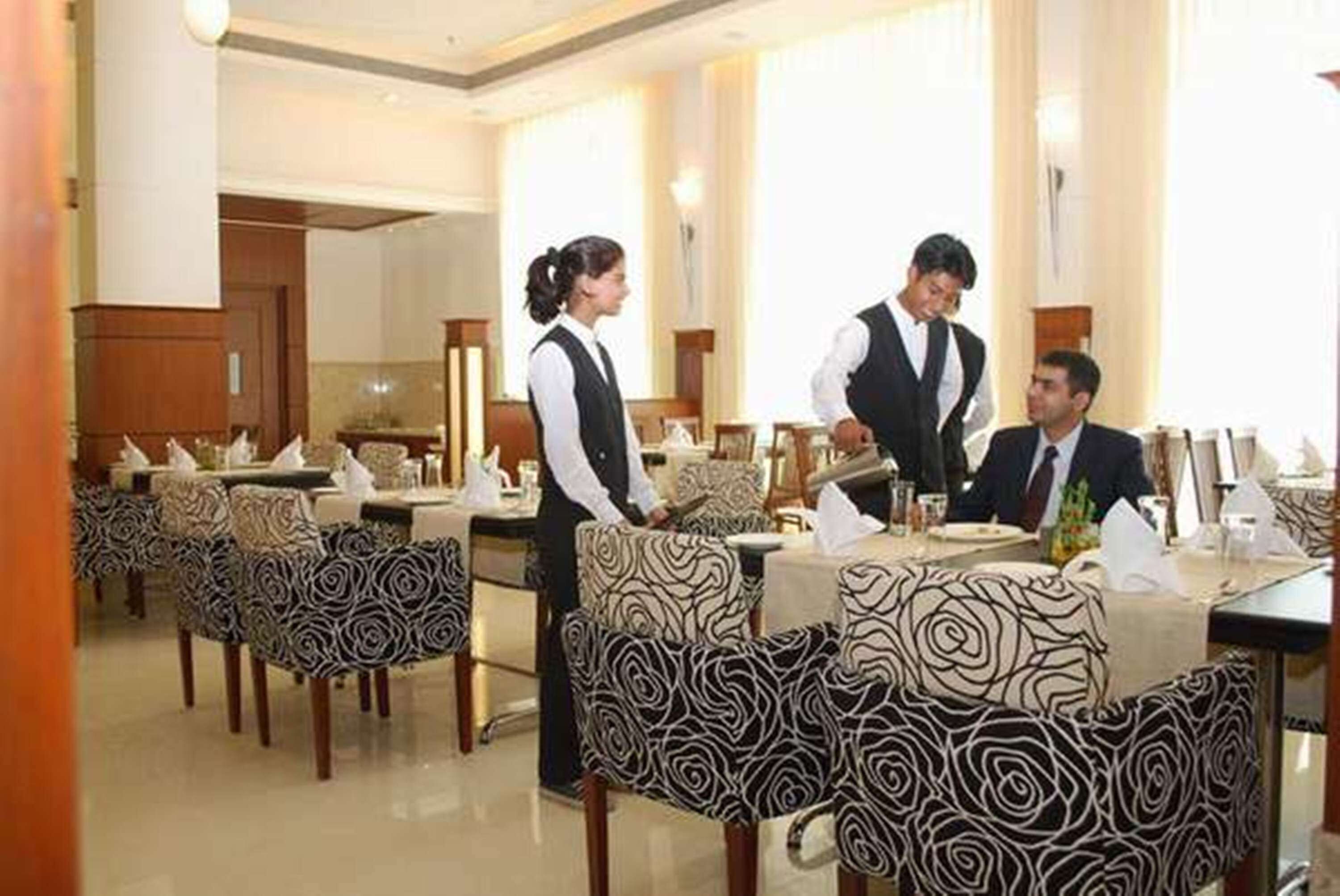 A restaurant with patterned chairs, a waiter, and a guest seated.