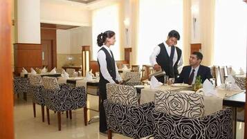 A restaurant with patterned chairs, a waiter, and a guest seated.