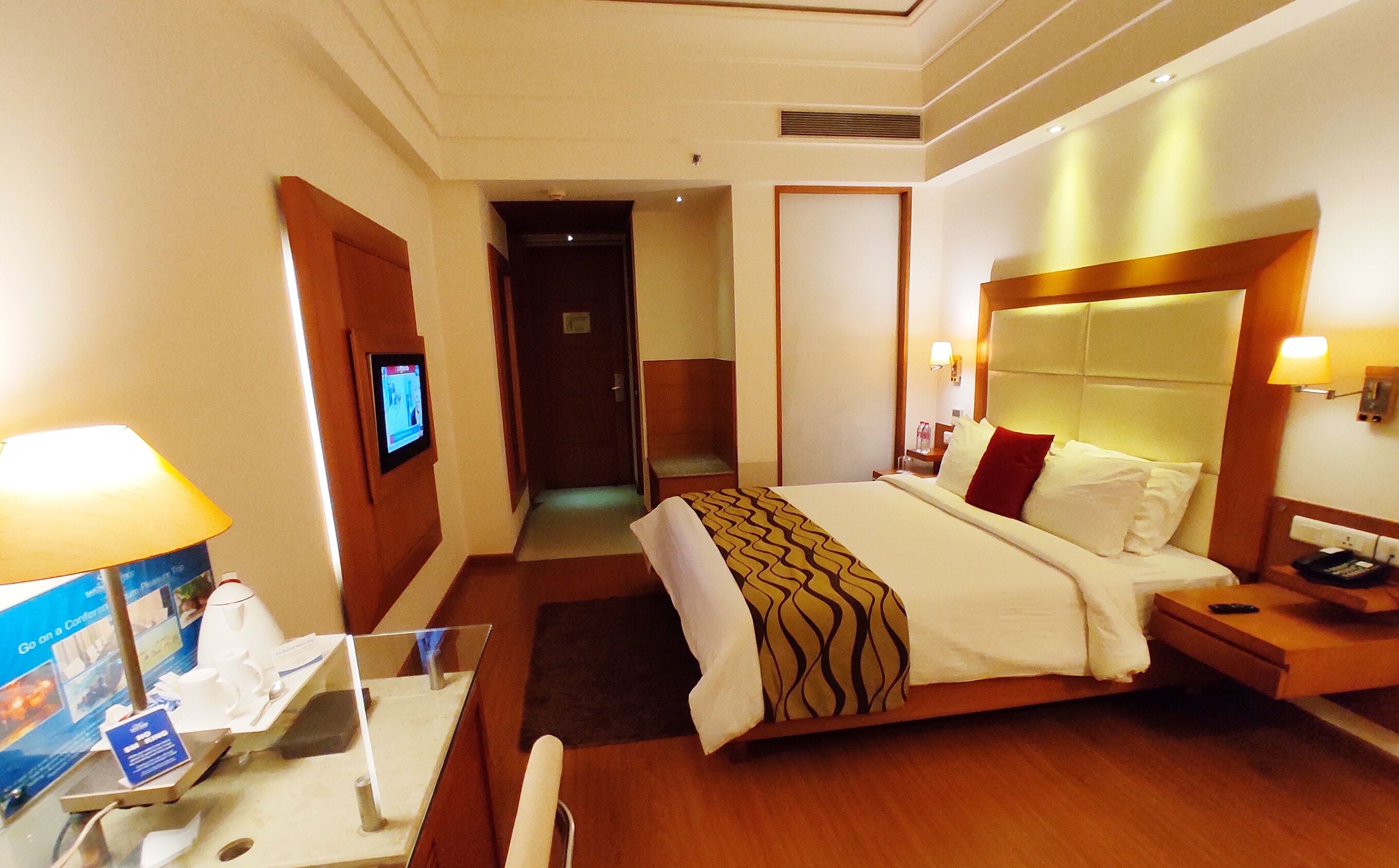 Una camera d'albergo con un letto, comodino, lampada, televisione e bagno visibile attraverso una porta aperta.