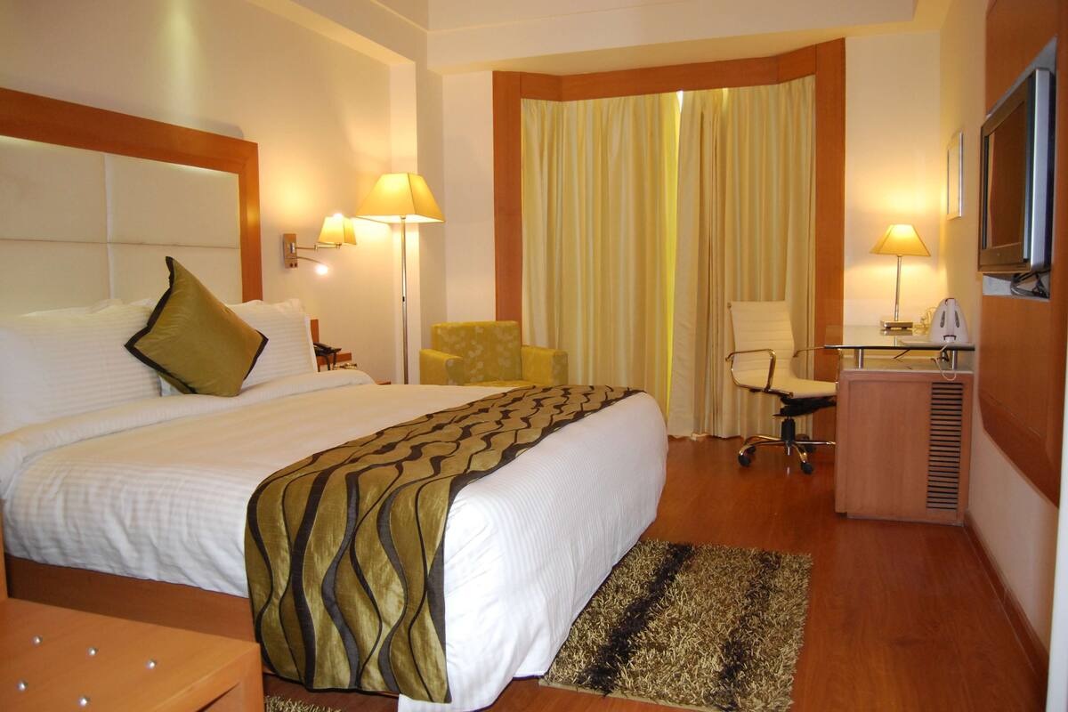 A hotel room with a large bed, a desk with a chair, a TV, and a window with curtains.