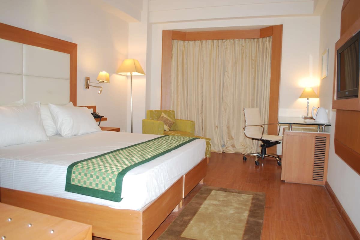 A hotel room with a large bed, a desk, a chair, a lamp, and a television.