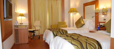 A hotel room with two beds, a desk, a chair, a television, and a bathroom.