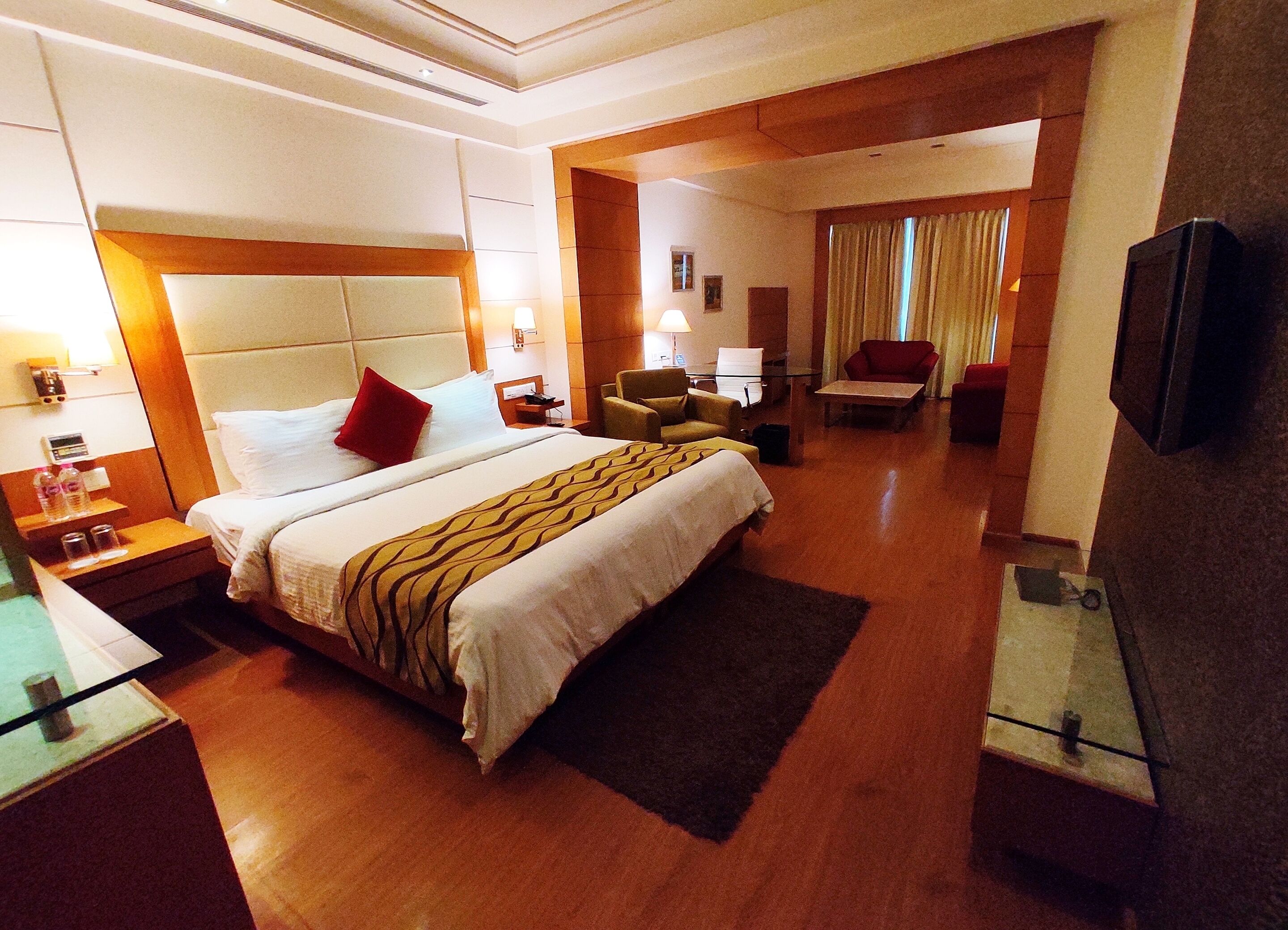 Quarto de hotel com uma cama grande, escrivaninha, cadeira, televisão e área de banheiro.