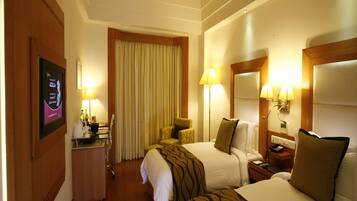 A hotel room with two beds, a desk with a computer, a chair, a lamp, and a TV mounted on the wall.