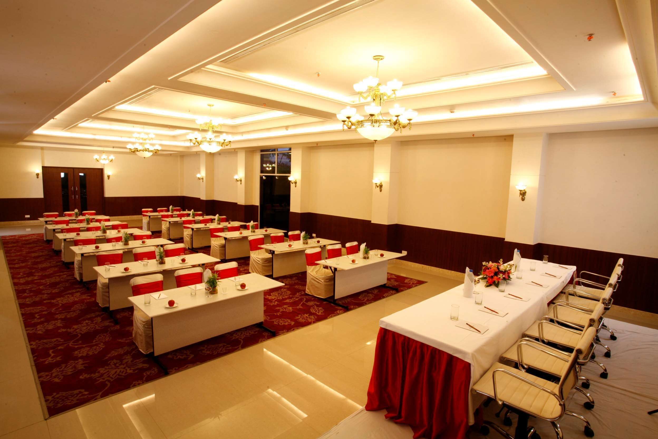 A conference room with multiple tables and chairs, red and white decor, and chandeliers.