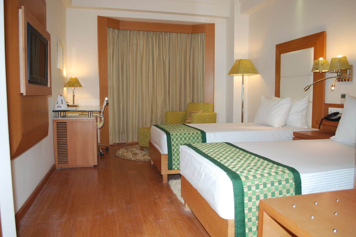 A hotel room with two beds, a desk with a lamp, a chair, and a mirror.