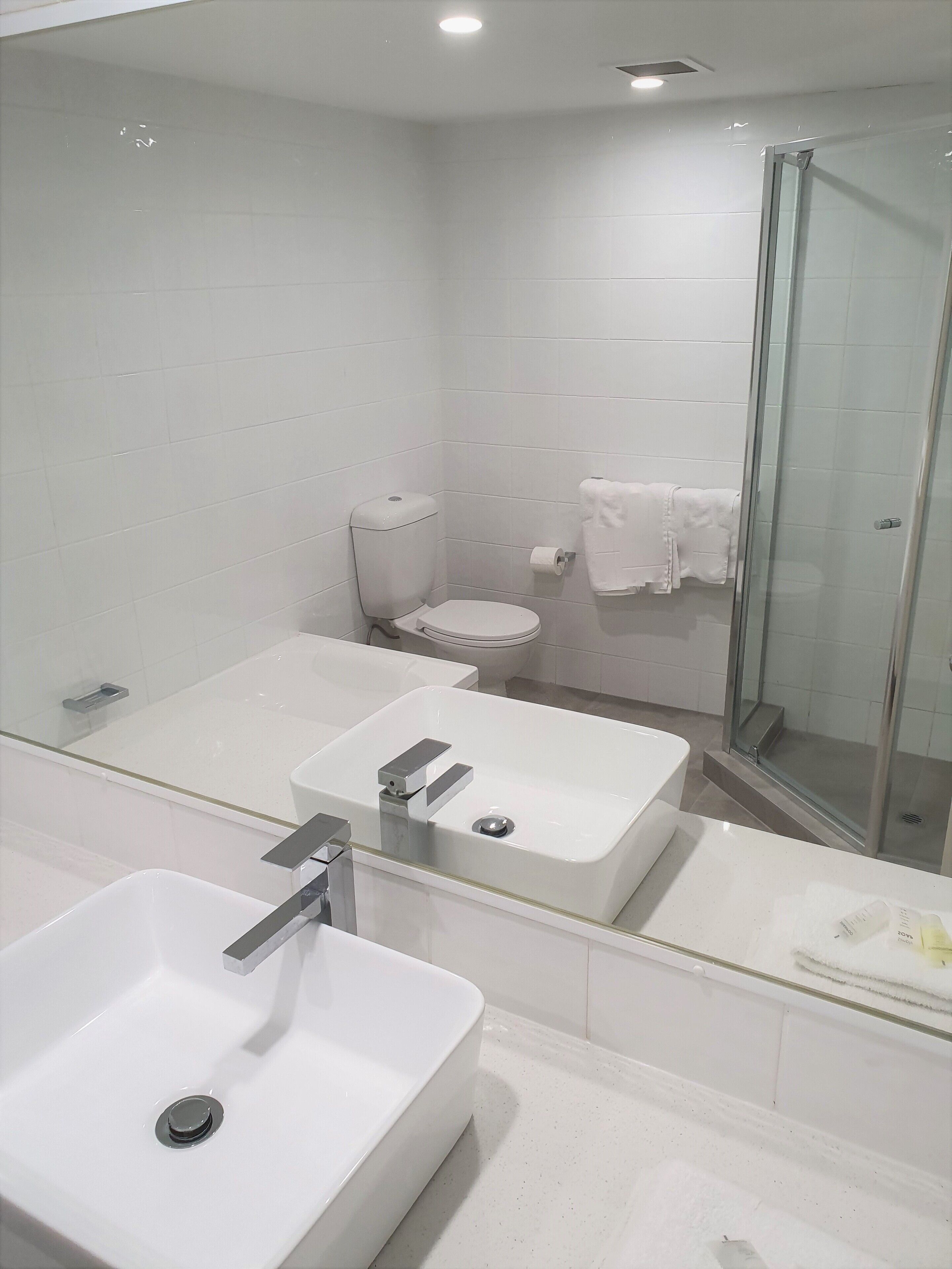 Een moderne badkamer met een grote spiegel, een wit wastafelmeubel, een toilet en een douchecabine met glazen wanden.