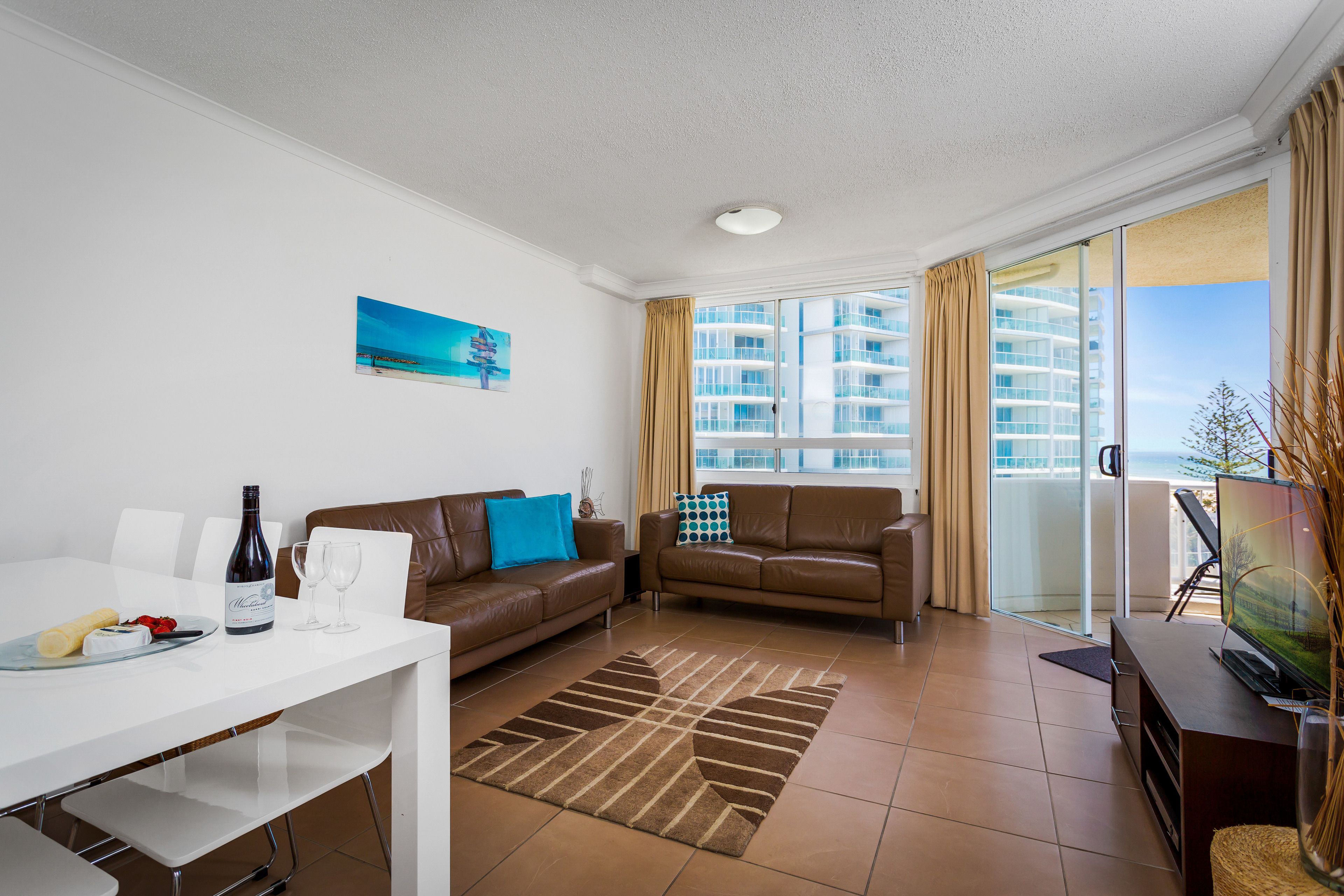 A modern living room with a dining table, sofas, a TV, and a large window with a view of high-rise buildings.