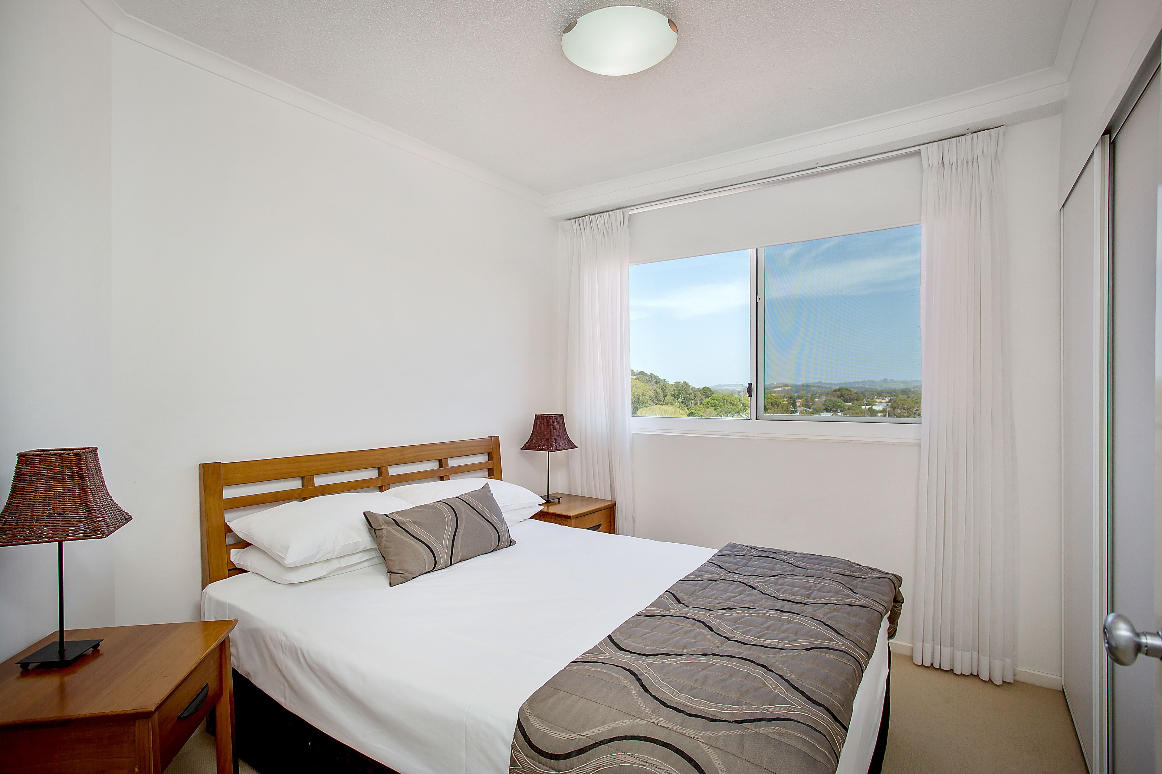 Una camera d'albergo con un letto, due comodini, una finestra con tende e vista sull'esterno.