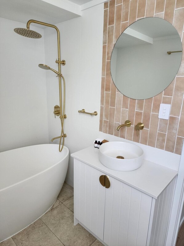 A bathroom with a freestanding bathtub, a vanity with a round sink, and a wall-mounted mirror.