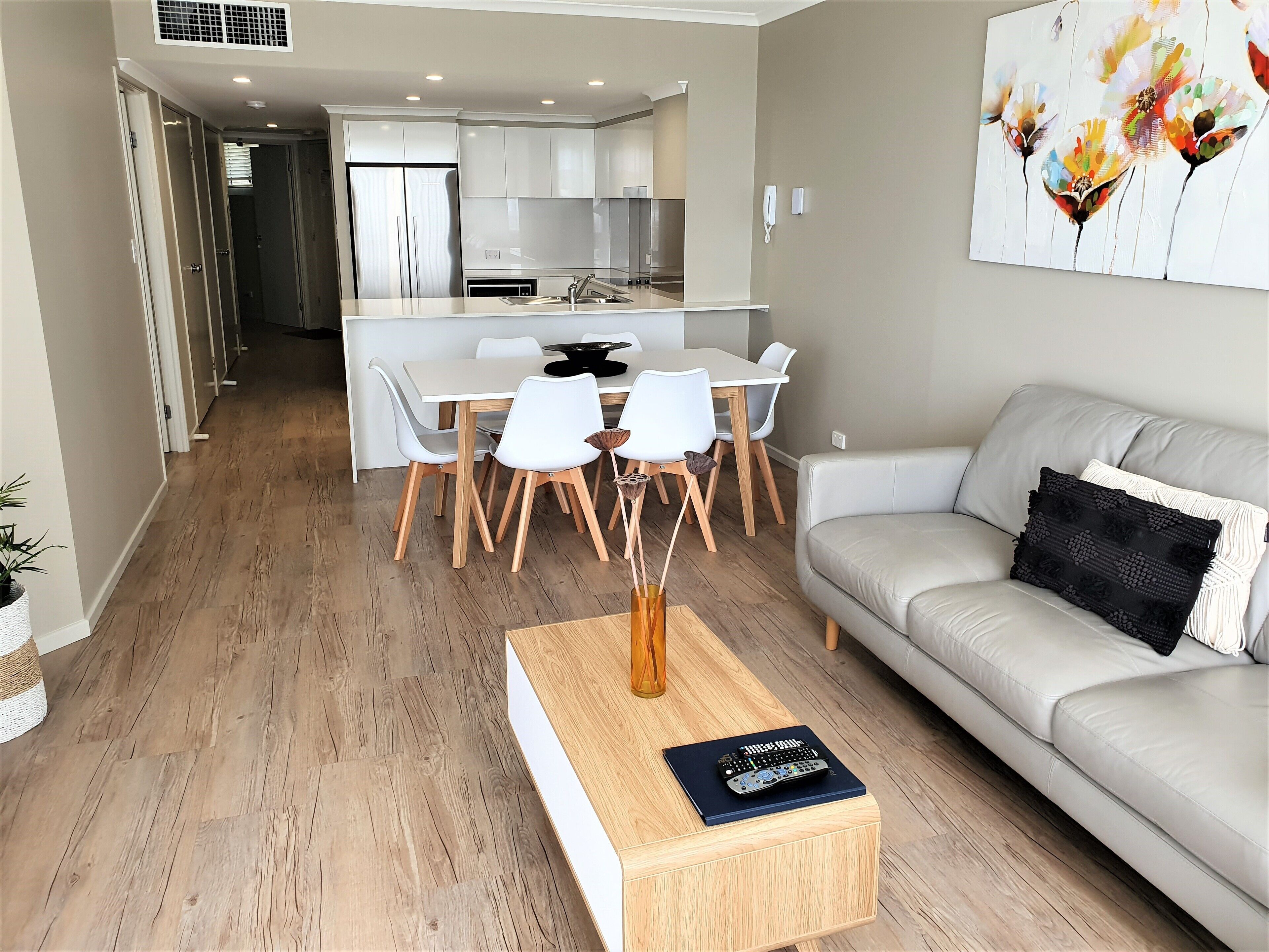 A modern living room with a grey sofa, a coffee table with a book, and a dining area with white chairs and a wooden table.