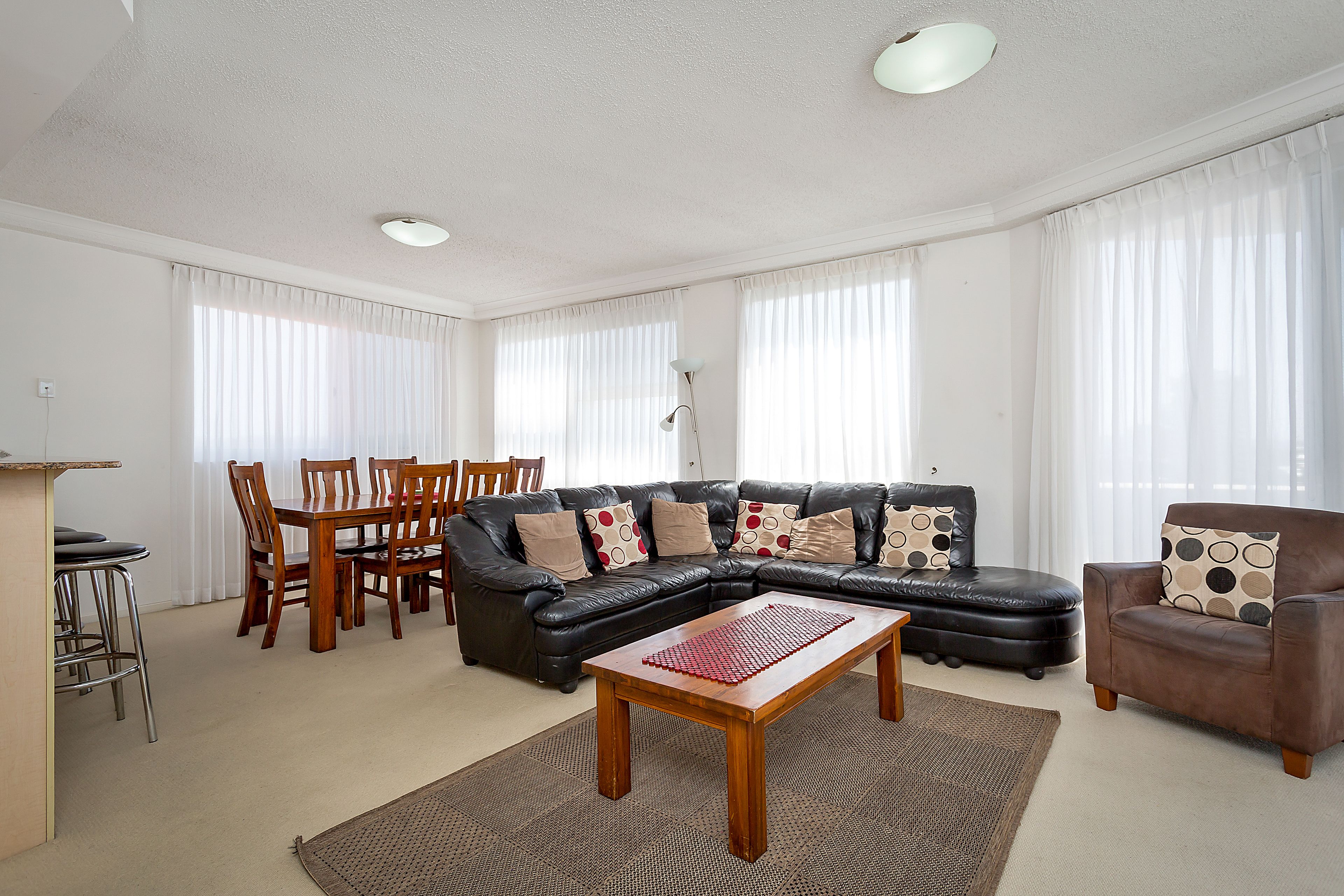 Una sala de estar con un sofá de cuero negro, una mesa de centro de madera y un comedor con sillas y una mesa.
