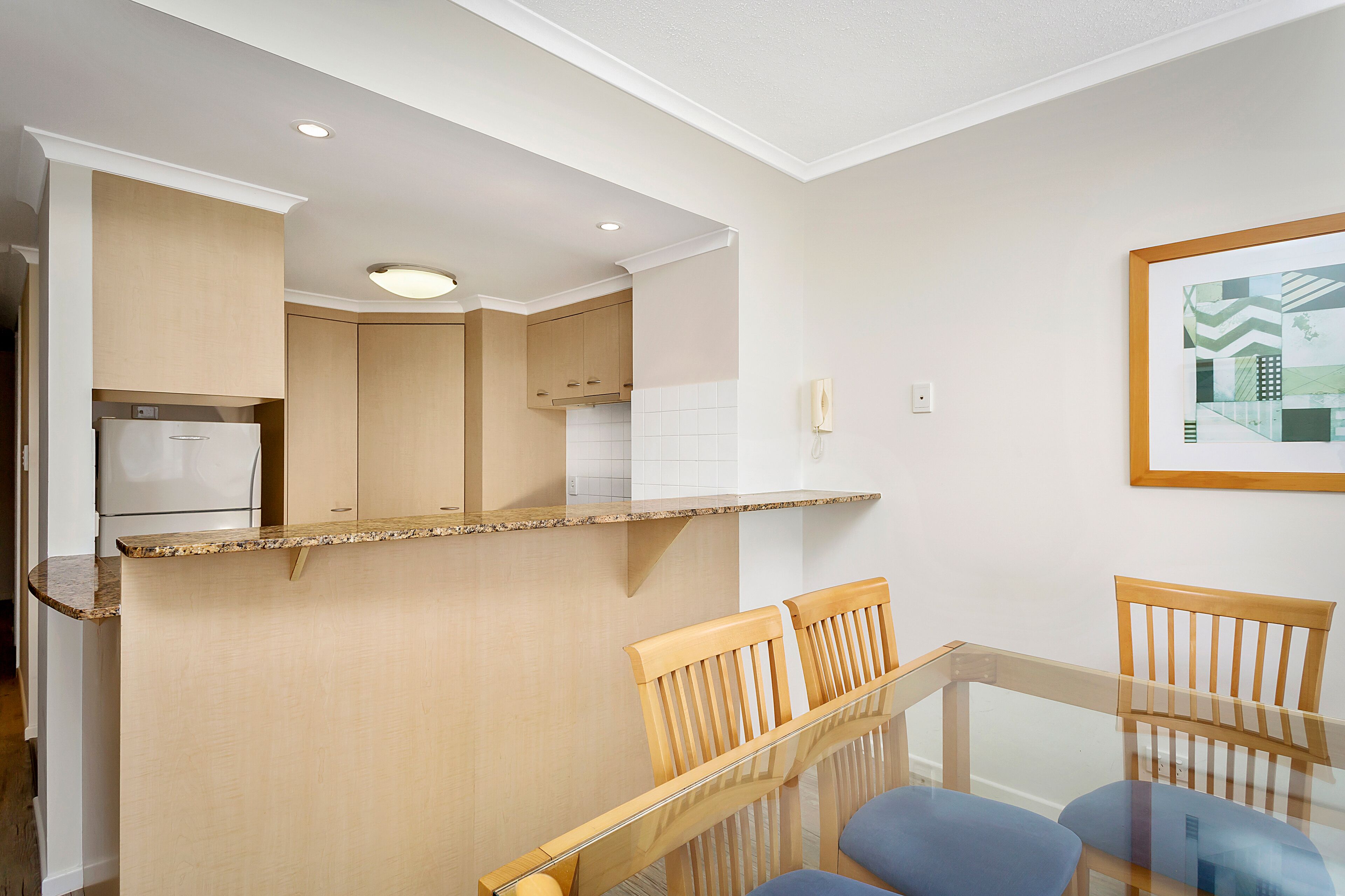A modern kitchen with a built-in refrigerator, wooden cabinets, and a glass dining table with chairs.