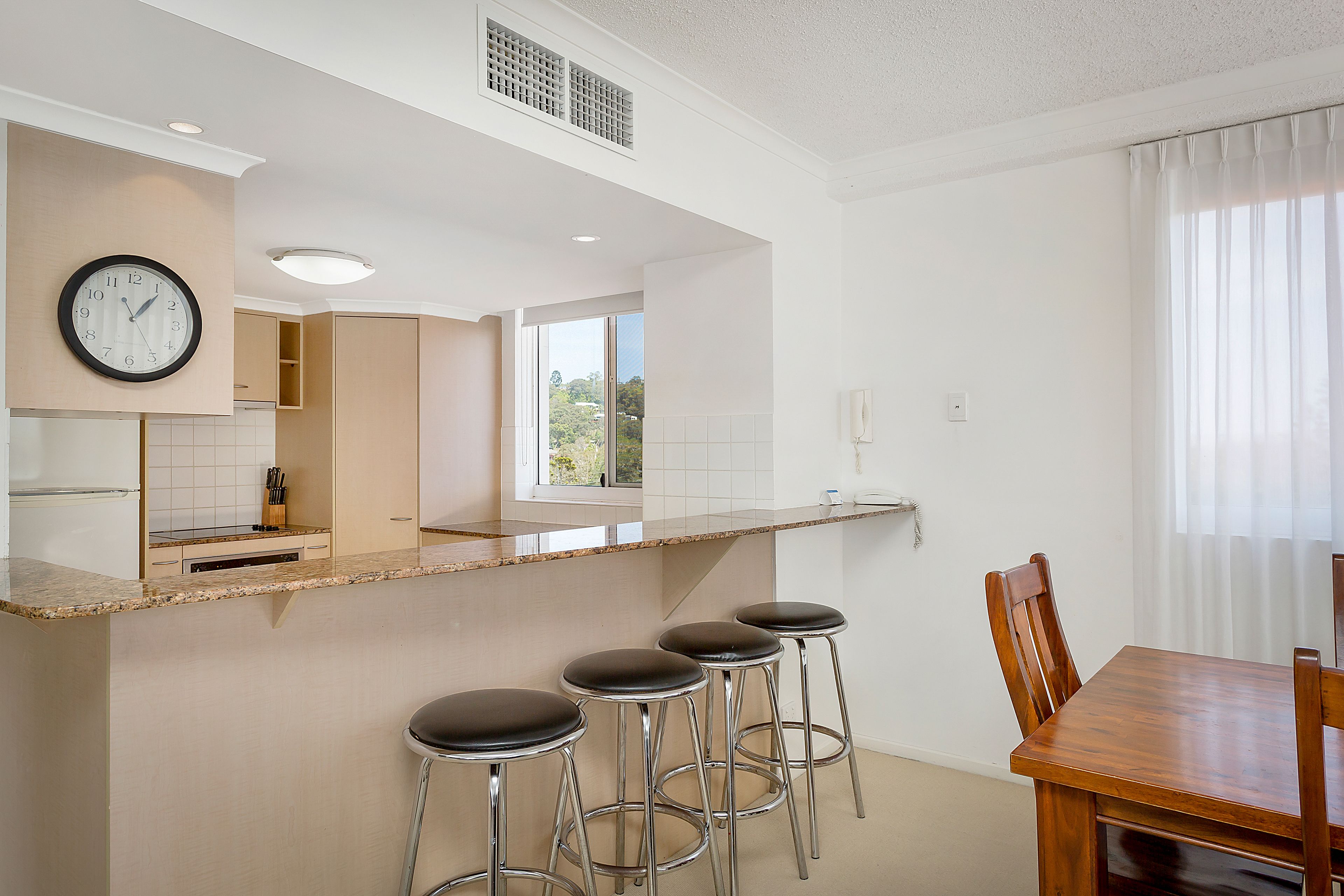 A modern kitchen with a bar area, a dining table, and a clock on the wall.