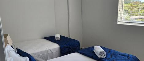 A room with two beds, a window with blinds, a door, and a ceiling vent.