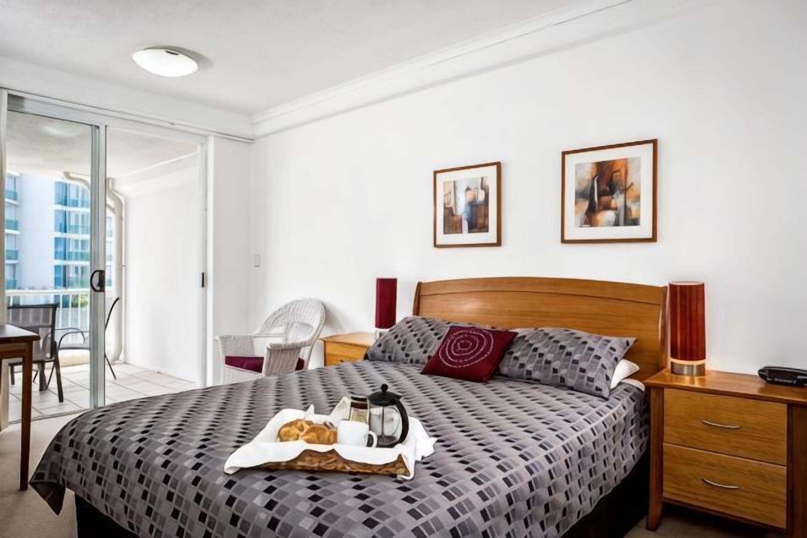 A bedroom with a bed, a bedside table, a chair, a desk, and a window.