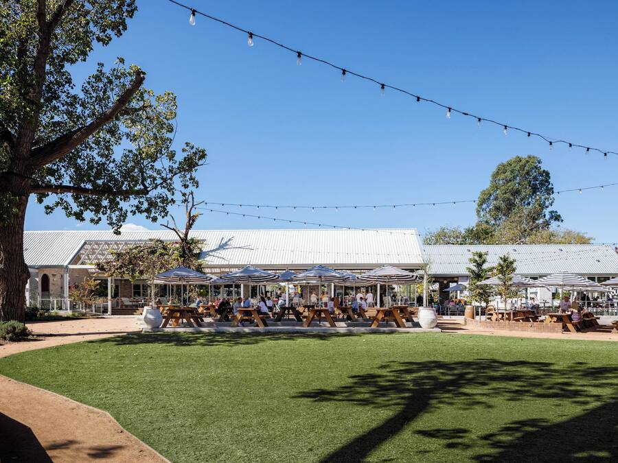 An outdoor seating area with tables and umbrellas, surrounded by trees and a building with a metal roof.