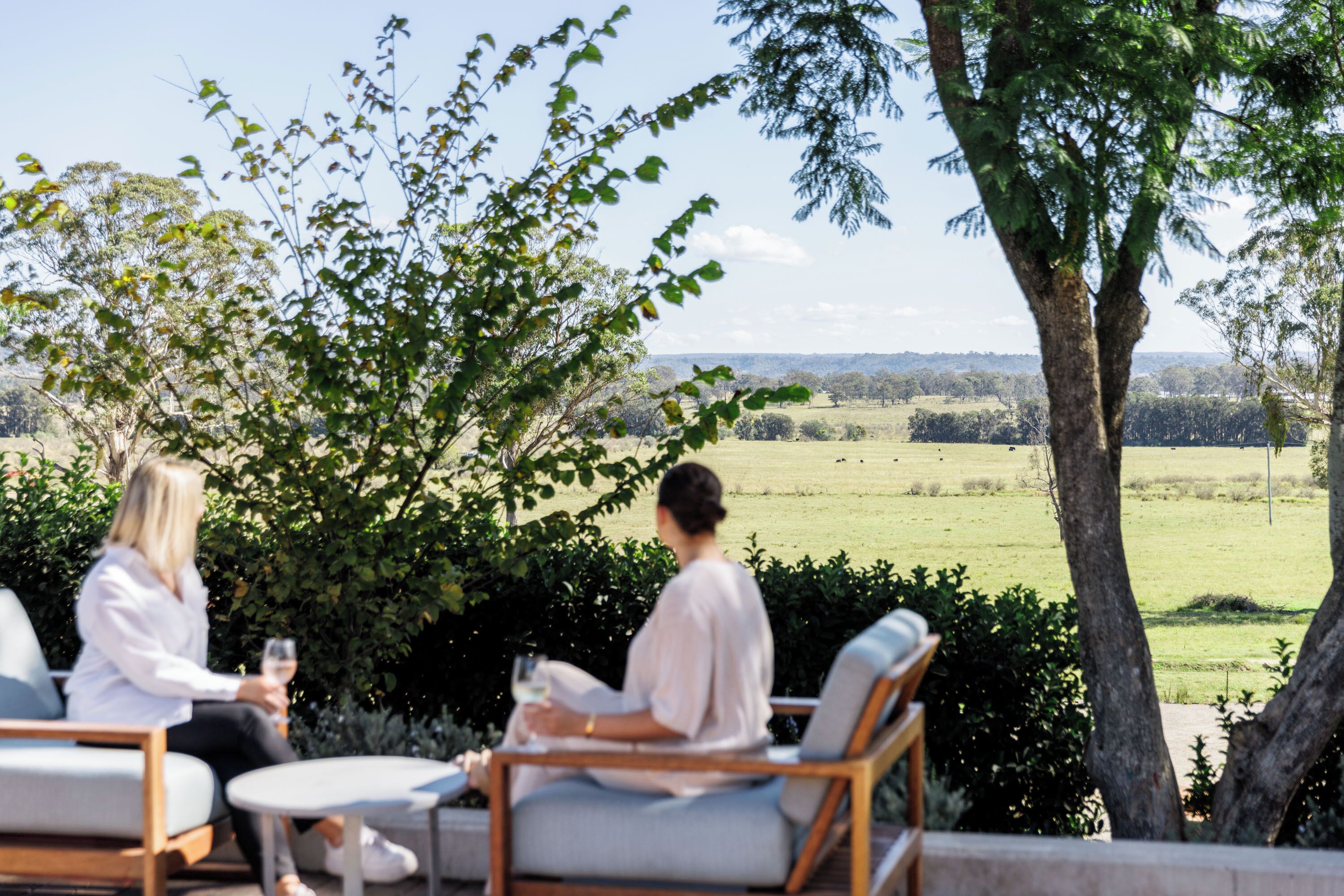 Two people sitting on outdoor furniture with a view of a grassy field and trees.