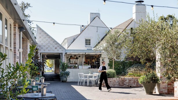 An outdoor cafe area with tables and chairs, a pathway, and a building with a white facade and a brick wall. - Camden Valley Inn (Cawdor)