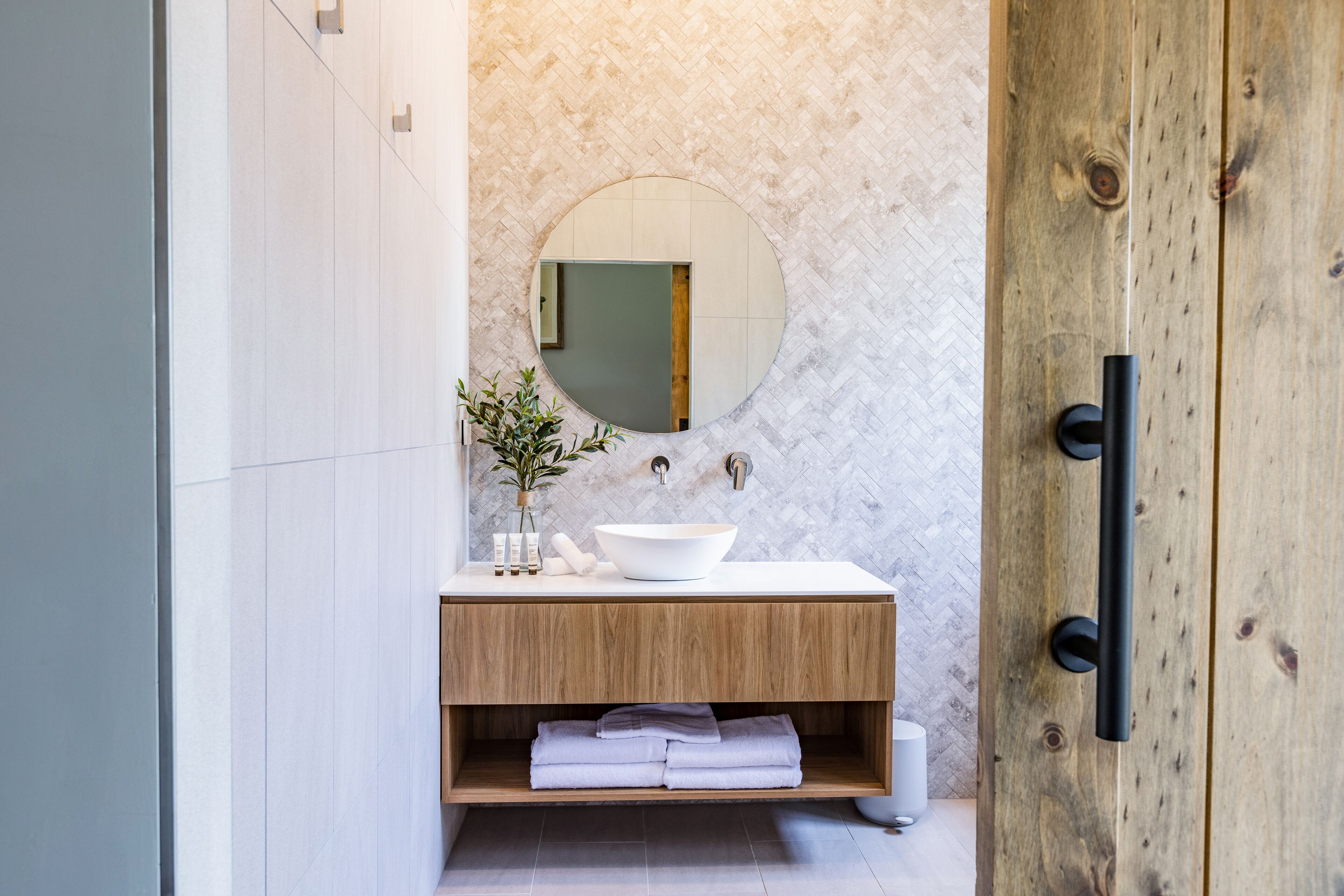 A modern bathroom with a wooden vanity, a round mirror, and a white sink.
