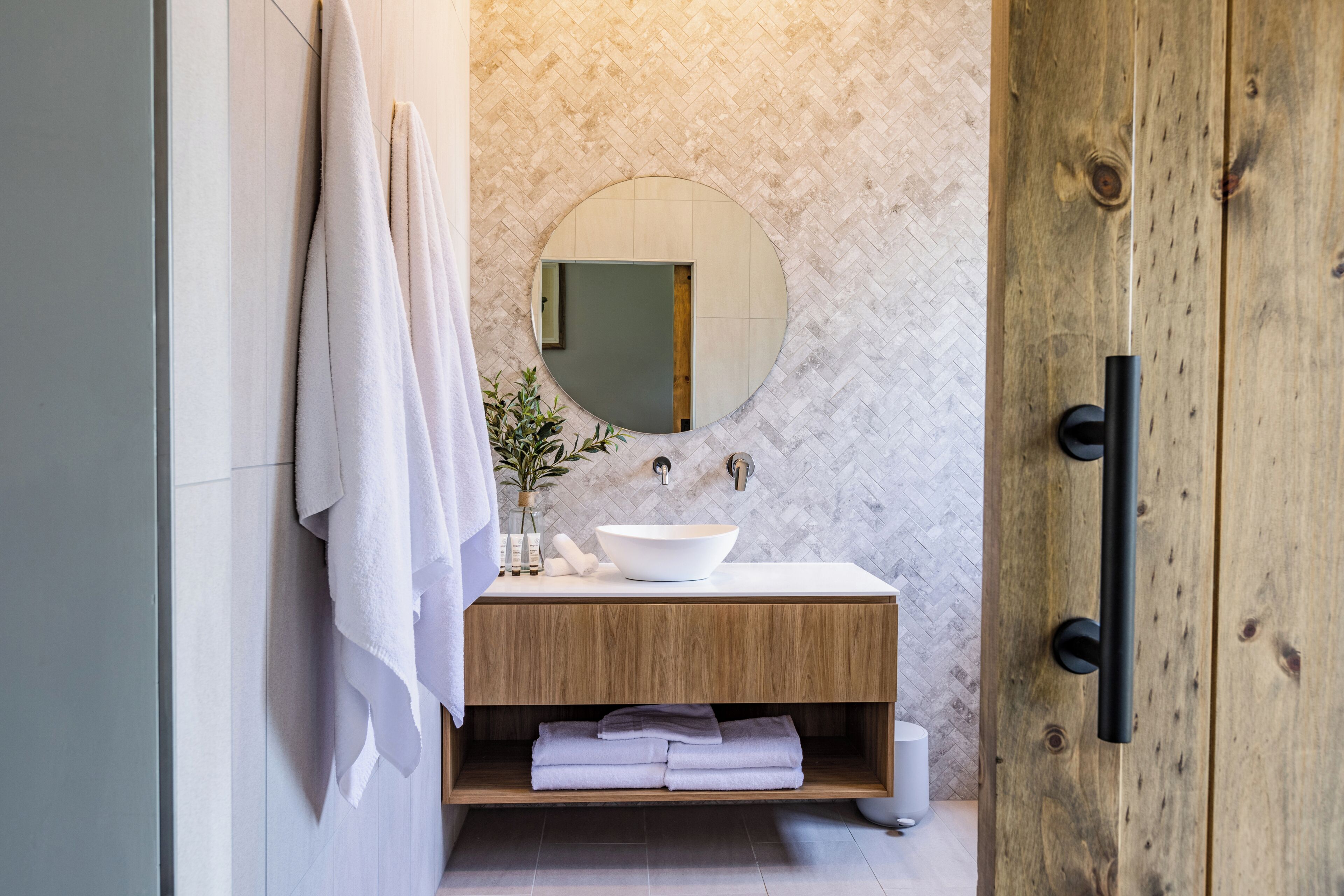 Un baño moderno con tocador de madera, espejo redondo y lavabo blanco.