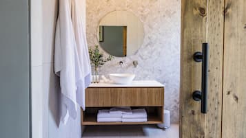 Un baño moderno con tocador de madera, espejo redondo y lavabo blanco.