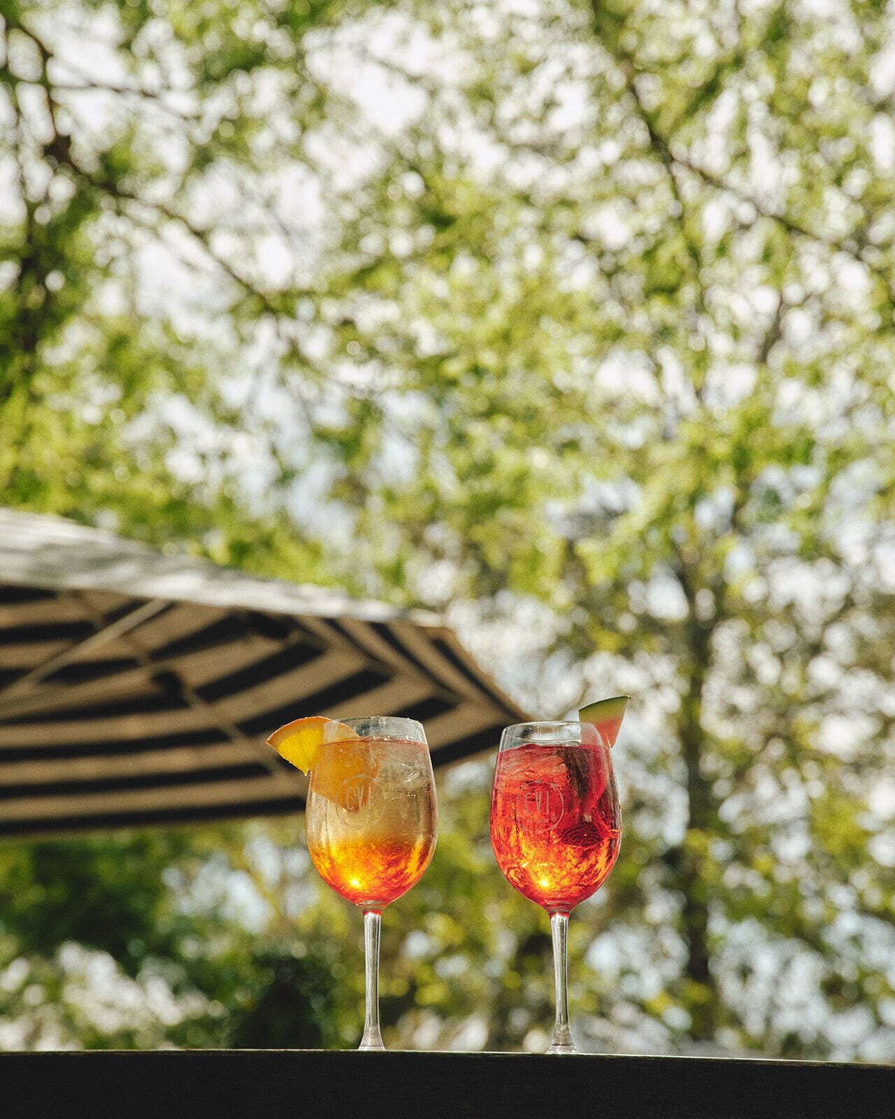 Two glasses of beverages on a balcony with a blurred background of trees.